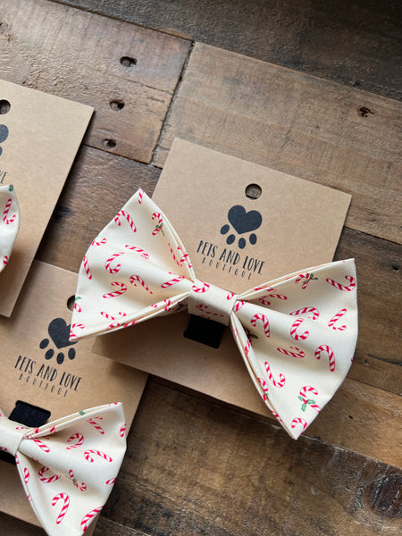 A cream-colored pet bow tie with a red and white candy cane print. The card is arranged on a rustic wooden surface alongside other cards and a matching bow tie.