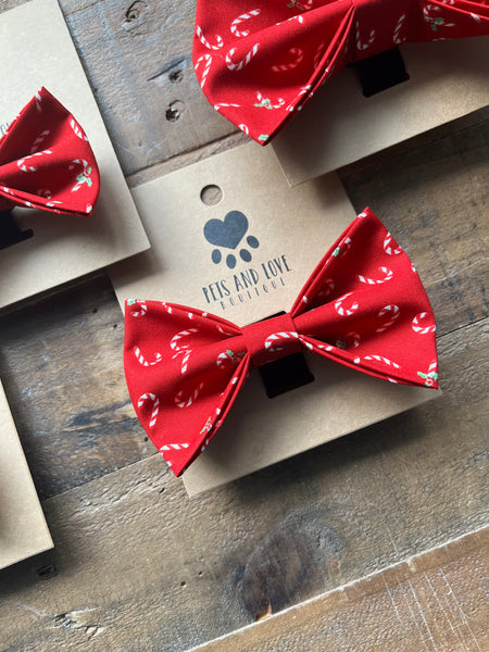 A red bow tie with a white candy cane pattern, displayed on a kraft paper card. 