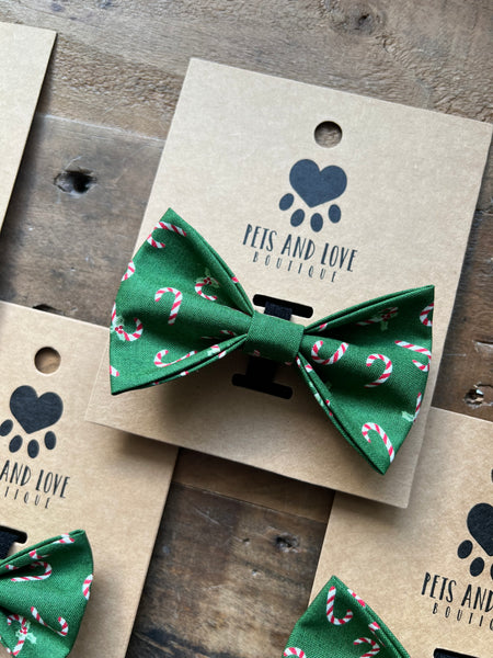 A green pet bow tie with a candy cane pattern, displayed on a brown kraft paper card printed with the brand name 'Pets and Love Boutique'.