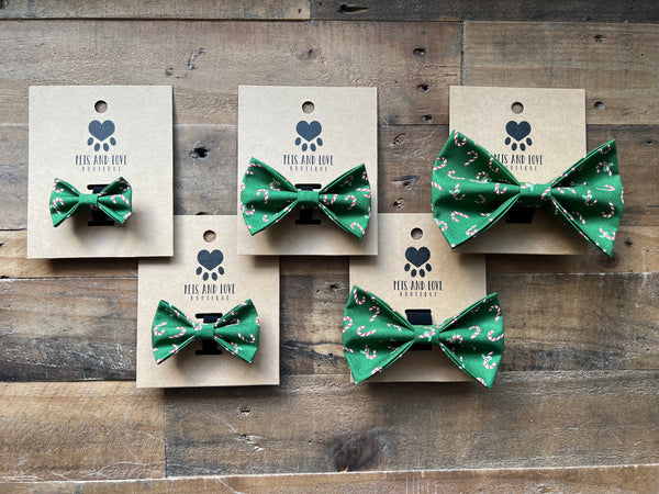Five green candy cane patterned bow ties displayed on kraft paper cards against a rustic wooden background. 