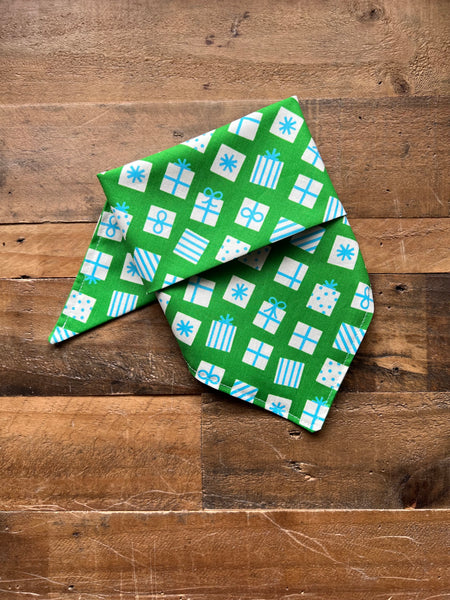 A green bandana with a white and blue gift box pattern, folded and displayed on a rustic wooden surface.