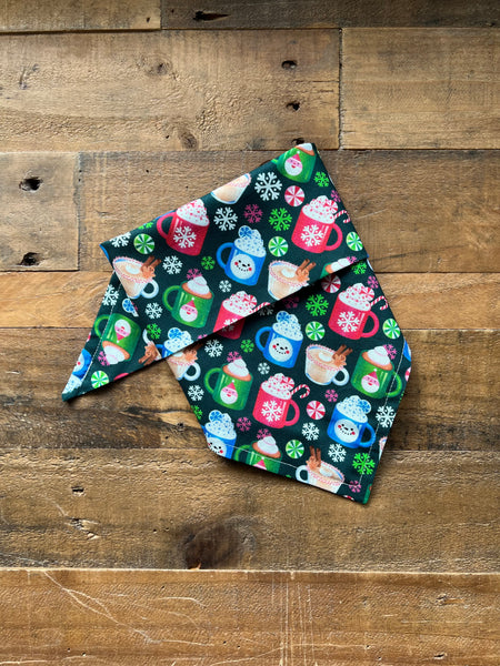 Fabric bandana with a festive holiday print of colorful coffee mugs, snowflakes, and candy canes on a dark background, displayed on a rustic wooden plank surface.