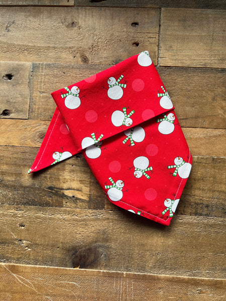A red bandana with a snowman print, laid flat on a rustic wooden surface.
