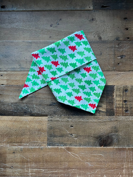 Dog Bandana with a green and red  Christmas tree pattern on a white background, displayed on a rustic wooden plank surface.