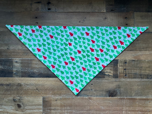 Dog Bandana with a green and red  Christmas tree pattern on a white background, displayed on a rustic wooden plank surface.