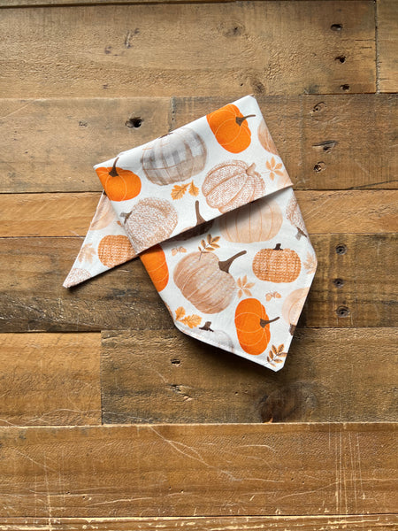 A folded bandana with an autumn pumpkin print, displayed on a rustic wooden plank surface.