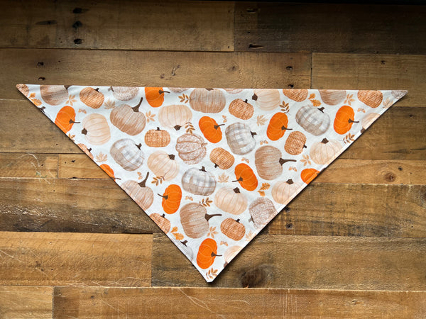 bandana with an autumn pumpkin print, displayed on a rustic wooden plank surface.