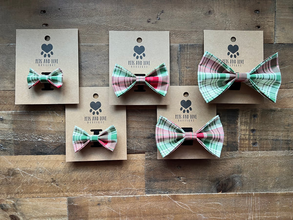Five pet collars with matching plaid bowties on kraft paper tags, displayed on a rustic wooden plank background. 