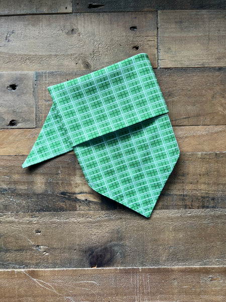 A green plaid bandana laid flat on a rustic wooden plank surface.