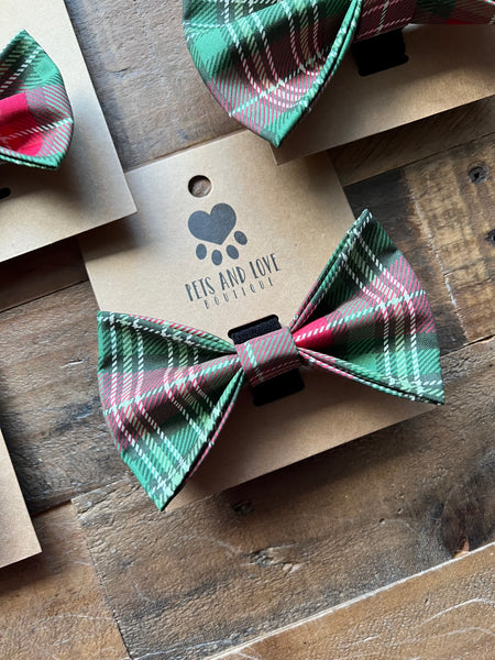 A large plaid pet bow tie in green, red, and white tartan, attached to a brown kraft paper display card.