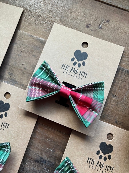 A medium plaid pet bow tie in green, red, and white tartan, attached to a brown kraft paper display card.