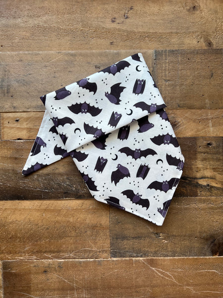 White Dog Bandana with black bat pattern on a wooden surface