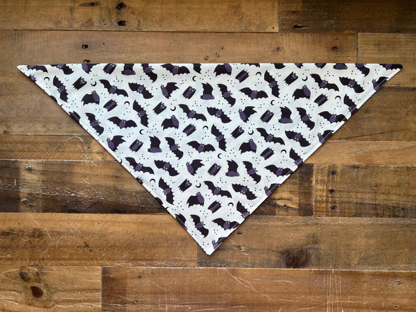 White Dog Bandana with black bat pattern on a wooden surface