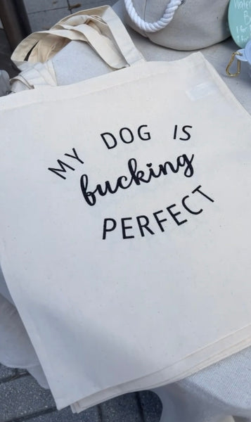 Cream Color tote bag with text 'My dog is fucking perfect' on a surface.