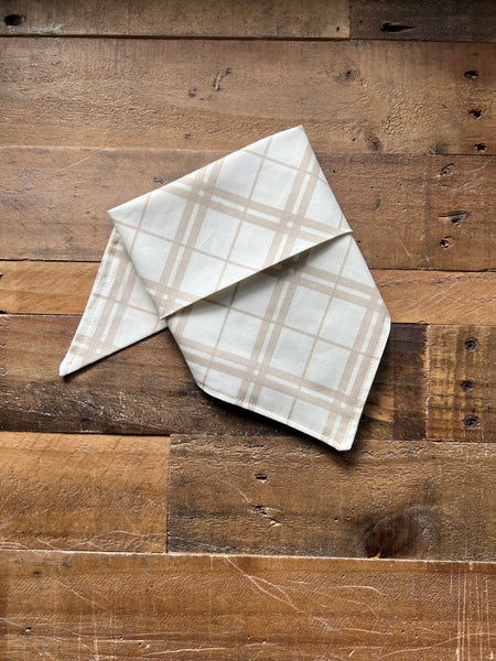 Dog bandana  with a beige plaid pattern, displayed on a rustic brown wooden plank surface.