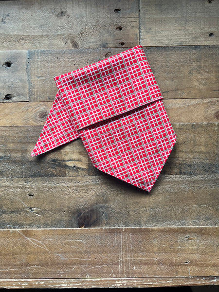 A red  green and white plaid bandana laid flat on a rustic wooden plank surface.