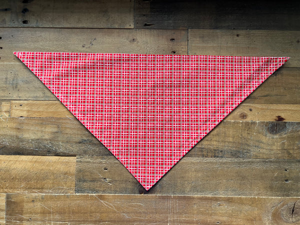 A red white green patterned triangular bandana, laid flat on a rustic wooden plank background.