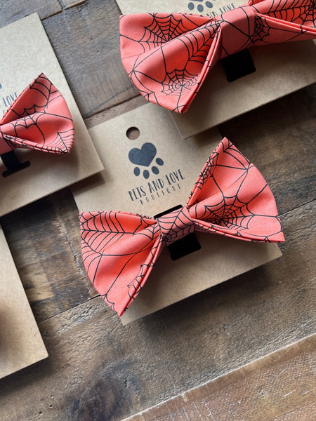 Orange bow ties with a black spiderweb pattern, displayed on brown kraft paper cards on a rustic wooden surface. 